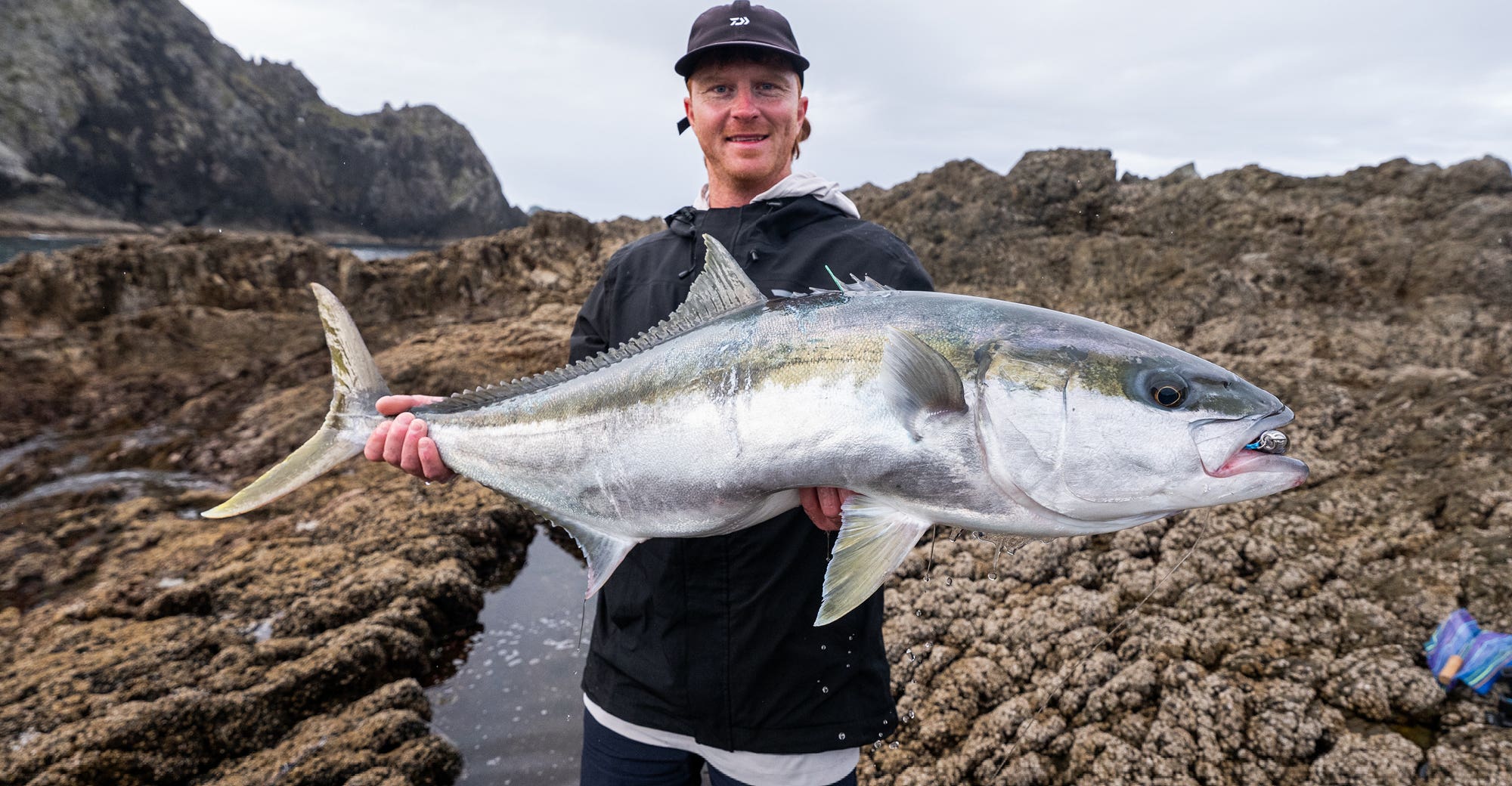 Man in a black jacket holding a large kingfish